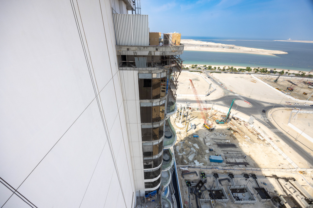Beach Walk Residence Construction site of a modern building overlooking a waterway, with cranes and machinery visible on the ground.